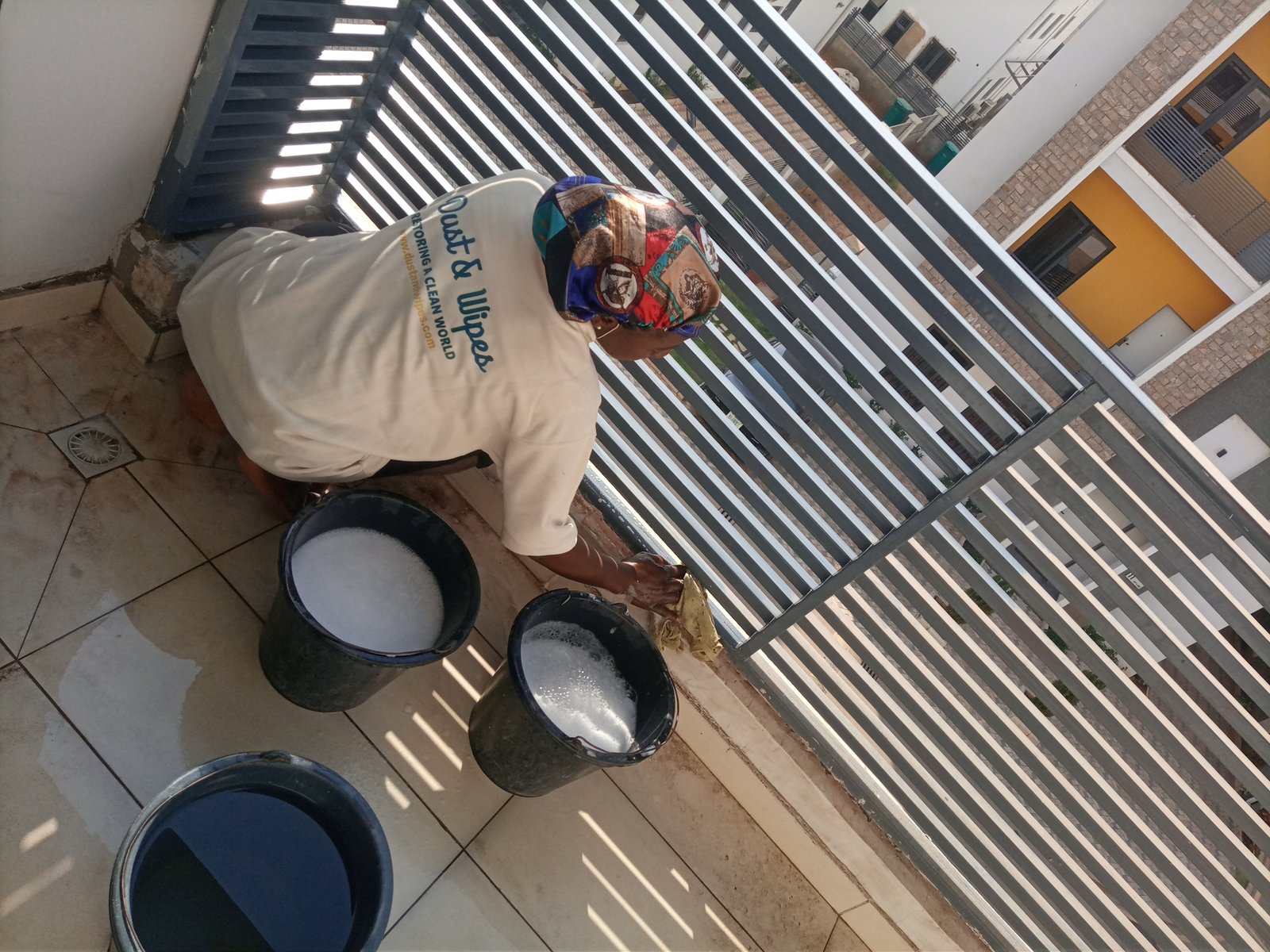 Dust and Wipes staff in cream uniform washing balcony with soapy buckets