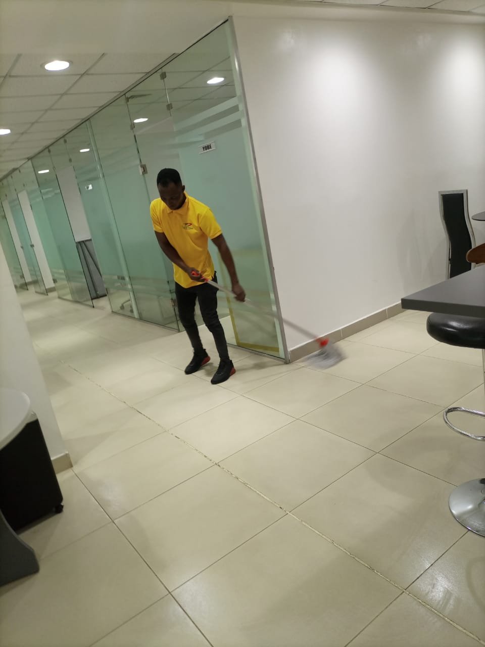 Male staff in yellow uniform sweeping glass-walled commercial office