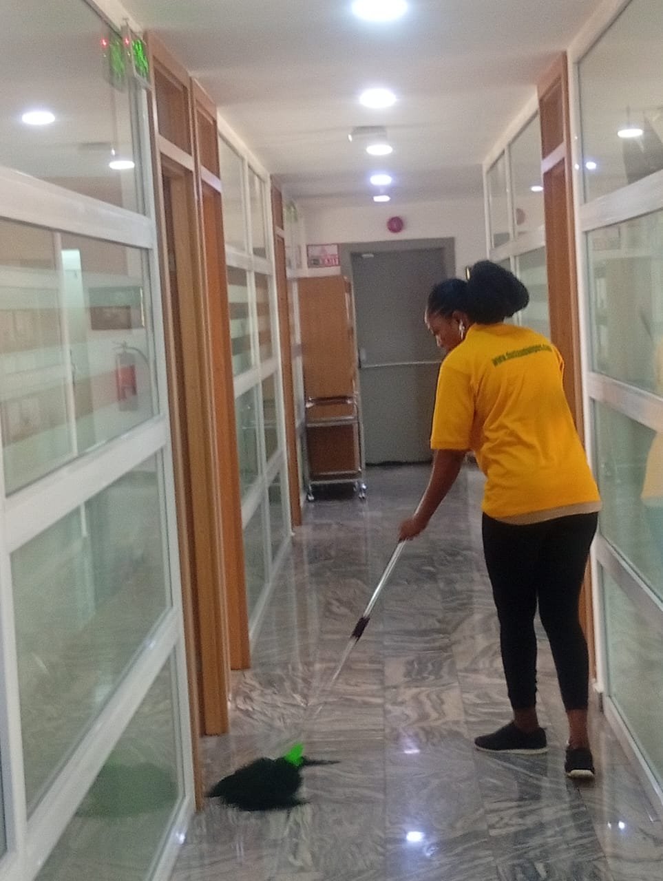 Dust and Wipes staff sweeping glass-partition office corridor in Abuja