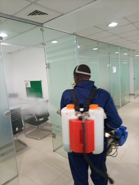 Dust and Wipes pest control technician in blue uniform fumigating glass-partition office