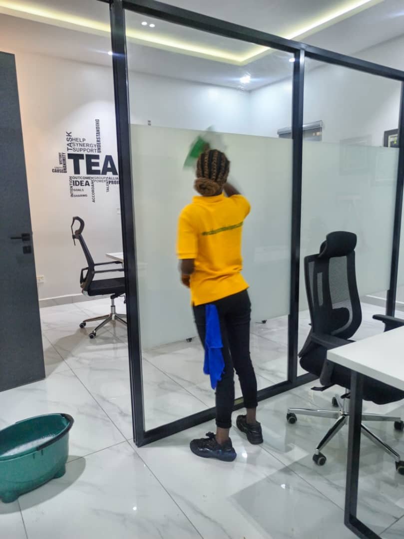 Female staff cleaning glass office partition with cloth and bucket