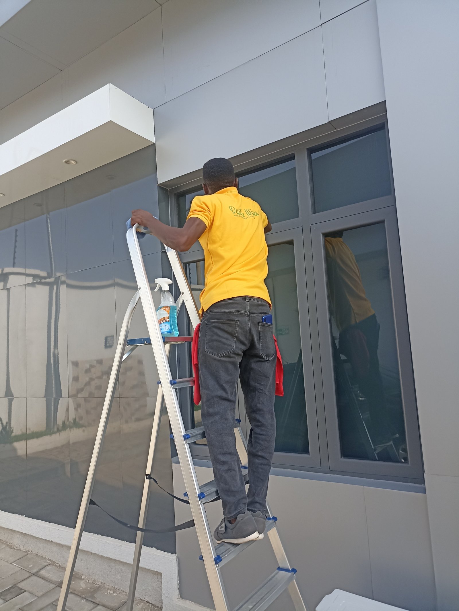 Dust and Wipes staff cleaning exterior windows on a ladder in Abuja